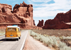 Urlaub mal anders: im VW-Bus reisen bedeutet Freiheit pur. Ein gelber alter Bulli fährt durch eine felsige Wüstenlandschaft.